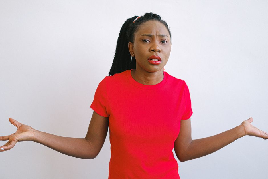Young black woman in a red shirt with a confused expression. Perfect for emotive stock photo needs.