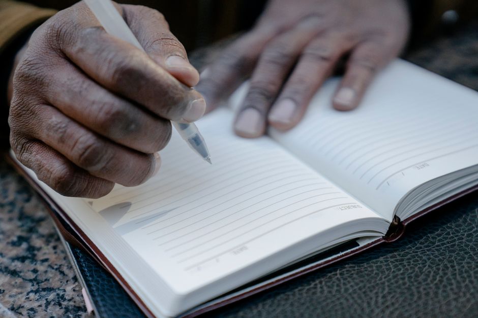 Hands writing with a pen in a notebook on a table, close-up view.