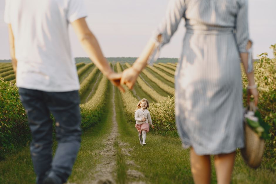 A family holds hands with their child in a beautiful, green field under a clear sky.
