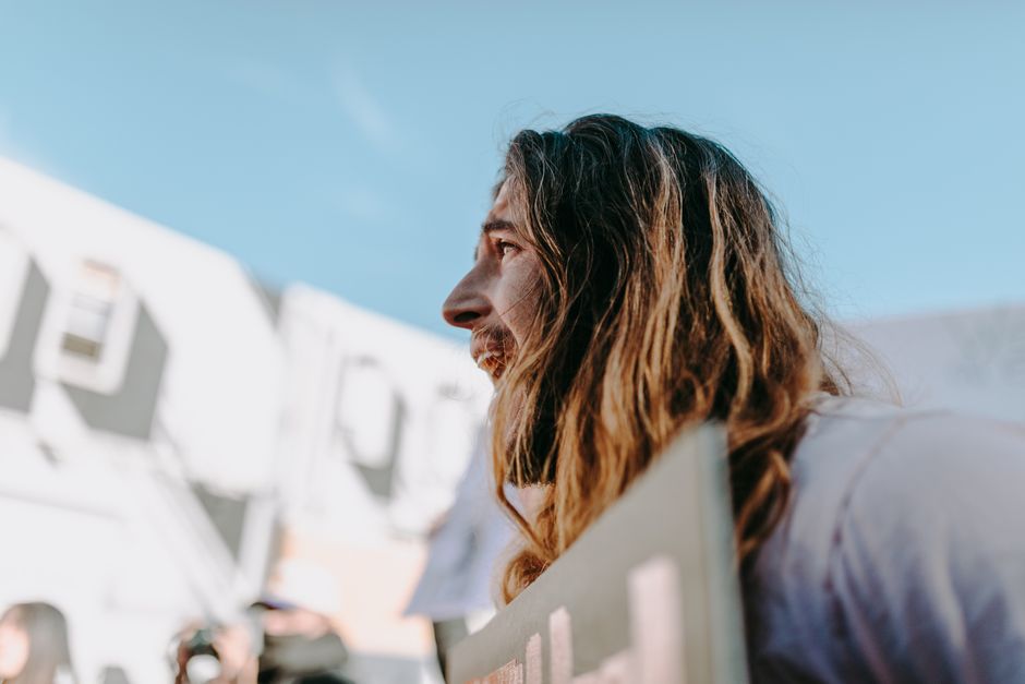 A man with long hair passionately engages in an outdoor protest, holding a sign.
