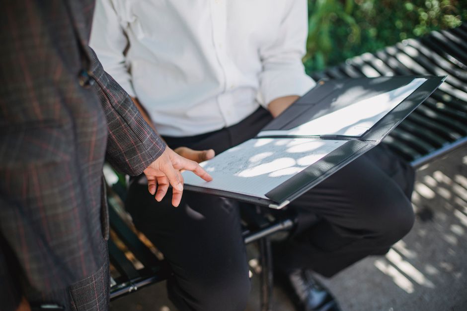 Two professionals in an outdoor setting reviewing documents on a bench.
